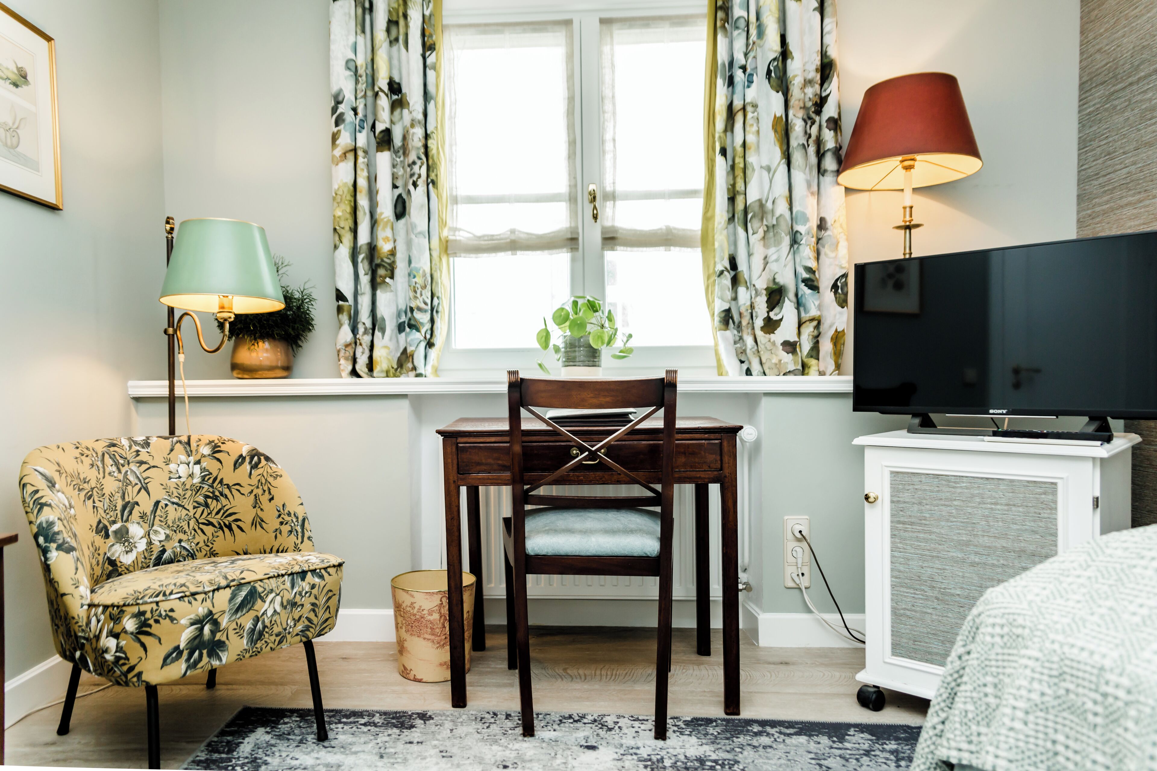 A room with a wooden chair, a small table, a television, and a window with curtains.