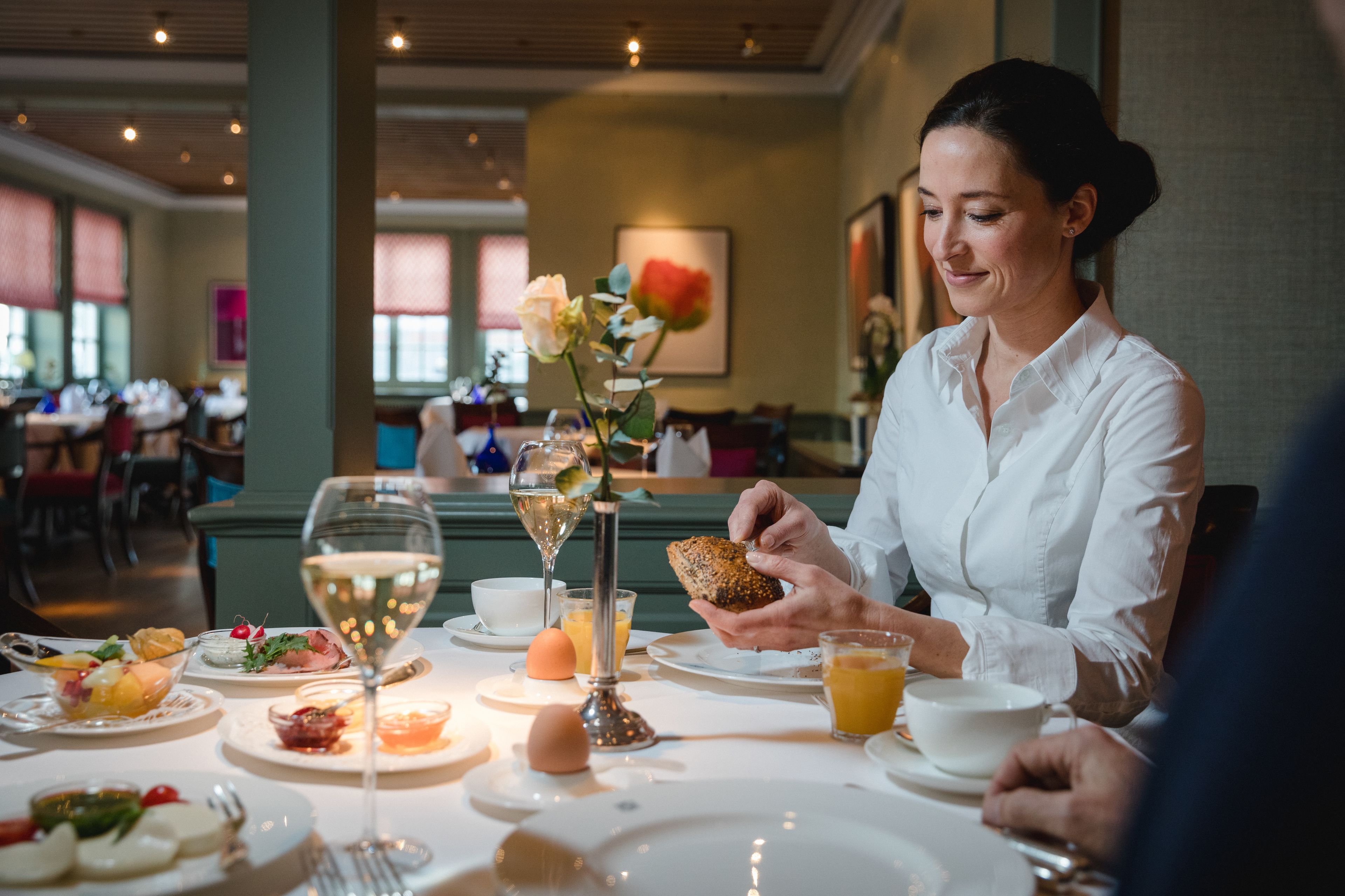 Une table à manger avec différents plats, un verre de vin blanc et un petit pain.