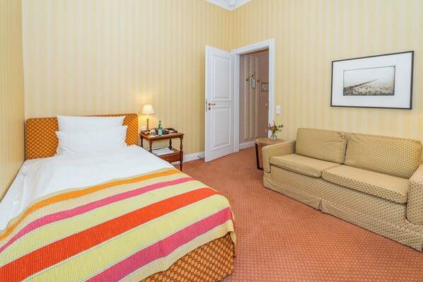 Habitación de hotel con cama, sofá, mesita de noche, lámpara y un cuadro en la pared.