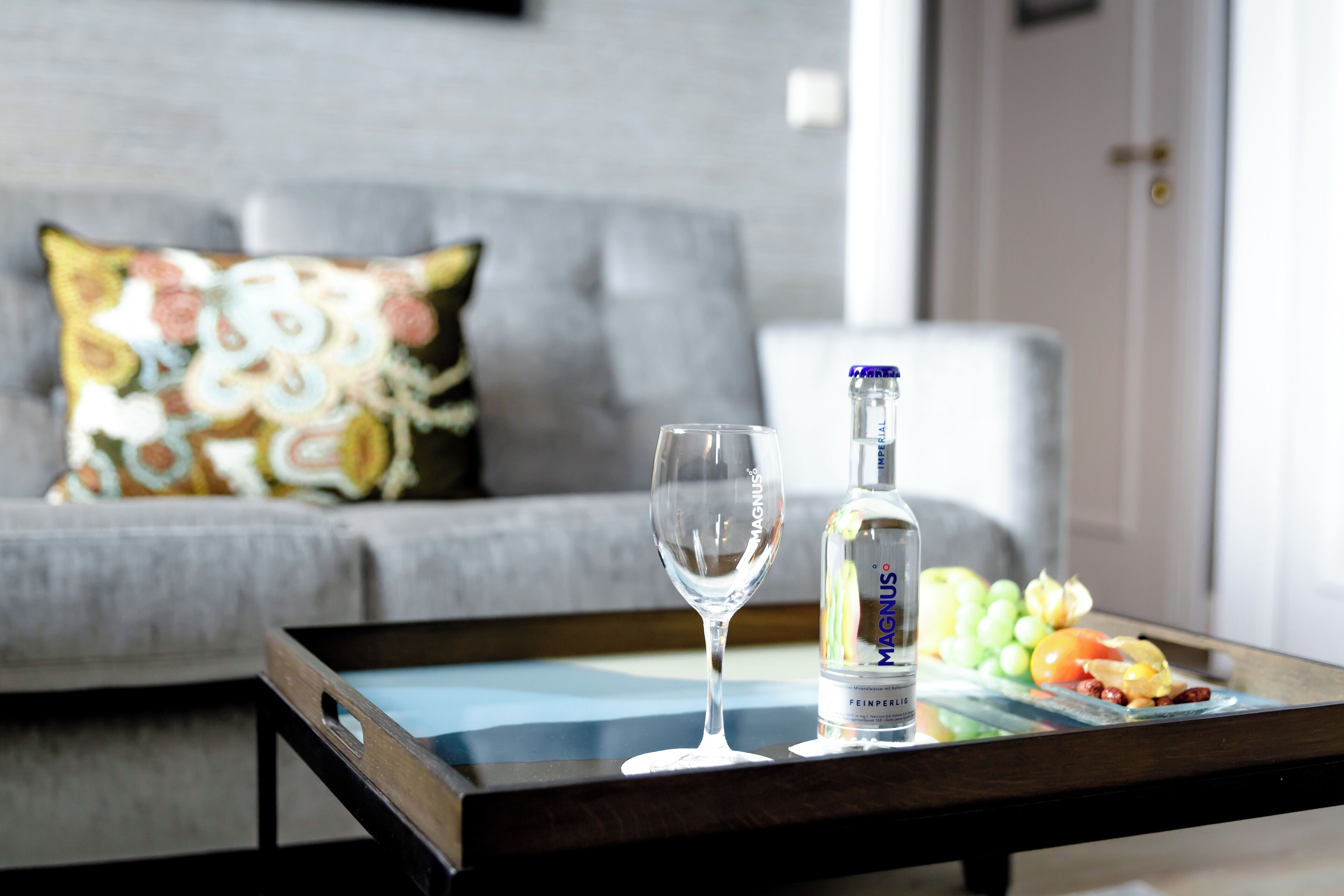 A glass of water, a bottle of Magnus, and a fruit platter on a tray.