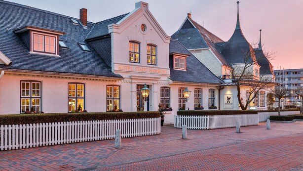 A historic building with a sign reading "HOTEL STADT HAMBURG" and a white picket fence in front. - Hotel Stadt Hamburg (Sylt)