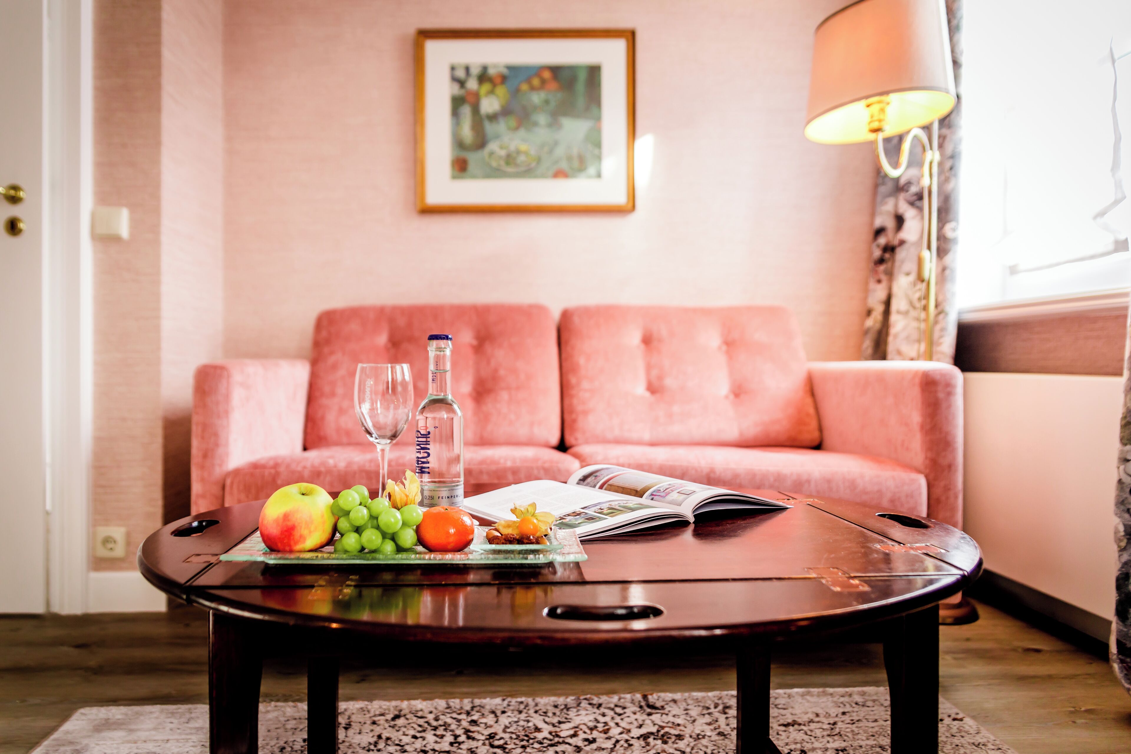 Una sala de estar con un sofá rosa, una mesita de centro con fruta y una revista, y una lámpara.