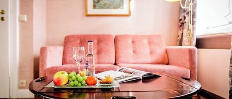 Una sala de estar con un sofá rosa, una mesita de centro con fruta y una revista, y una lámpara.