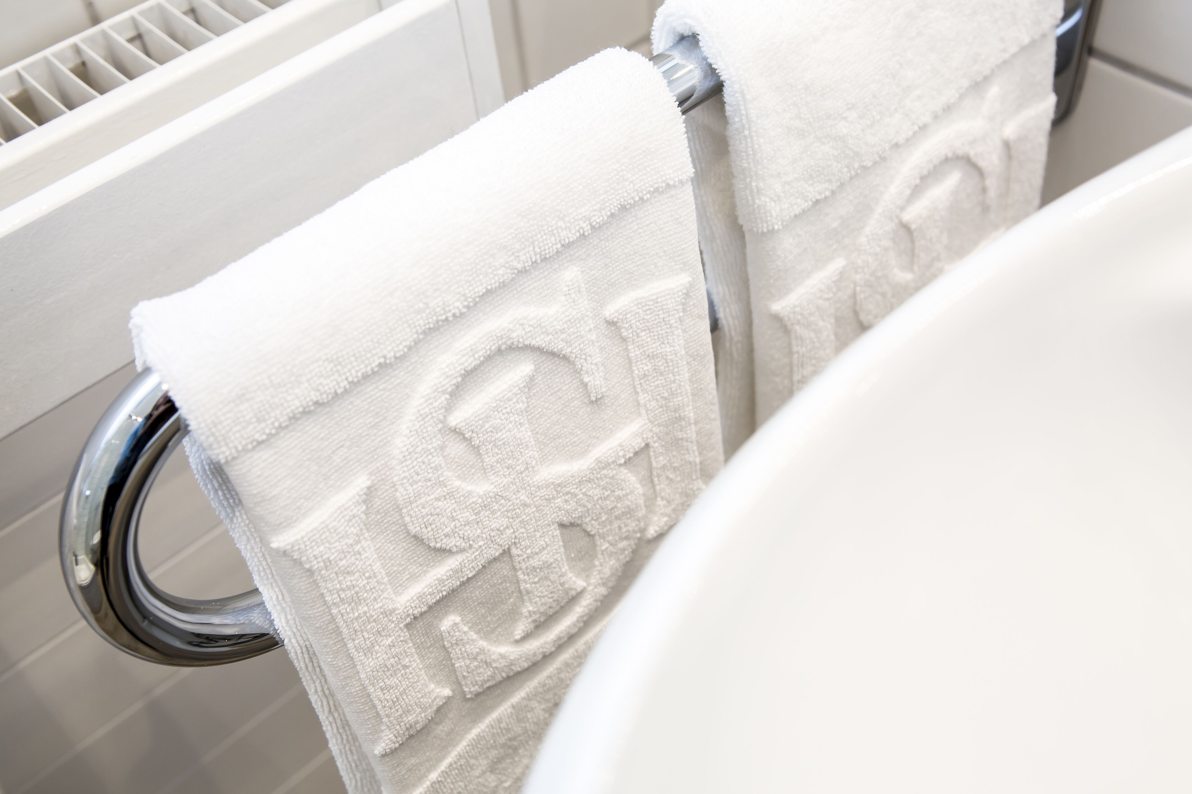 Une serviette blanche ornée d’un logo, posée sur un porte-serviettes en métal dans une salle de bain.