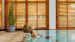 A person relaxing in a pool with wooden blinds in the background. - Hotel Stadt Hamburg (Sylt)