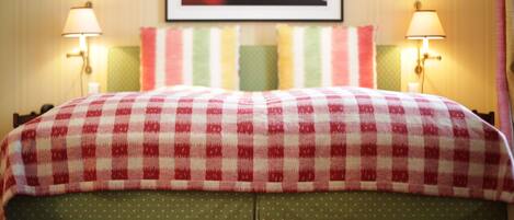 Una cama con colcha a cuadros rojos y blancos, fundas de almohada con lunares verdes y dos lámparas de noche.
