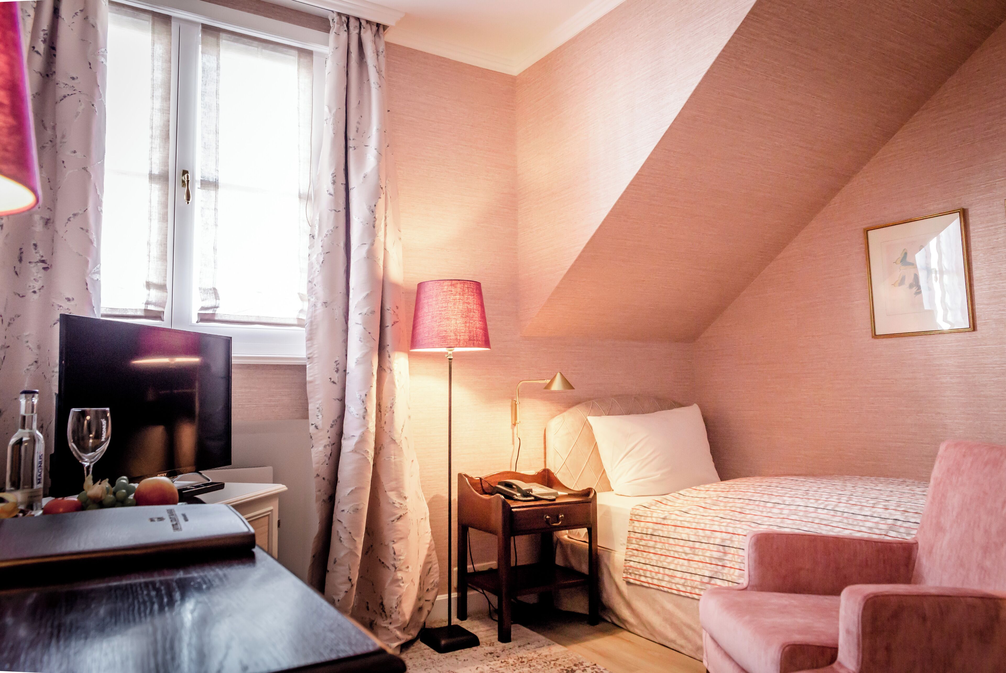A bedroom with a bed, a desk with a lamp, a TV, and a window with curtains.