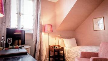 A bedroom with a bed, a desk with a lamp, a TV, and a window with curtains.