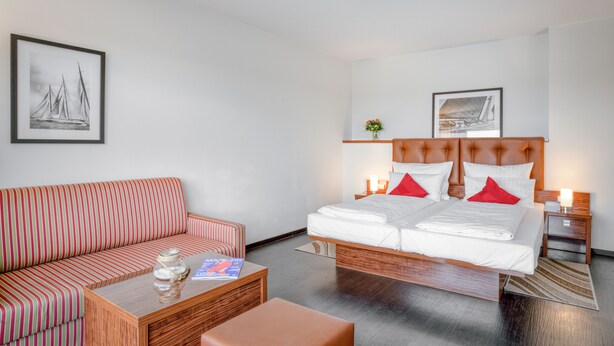 Een hotelkamer met een bed, een bank, een bijzettafeltje en twee schilderijen aan de muur.