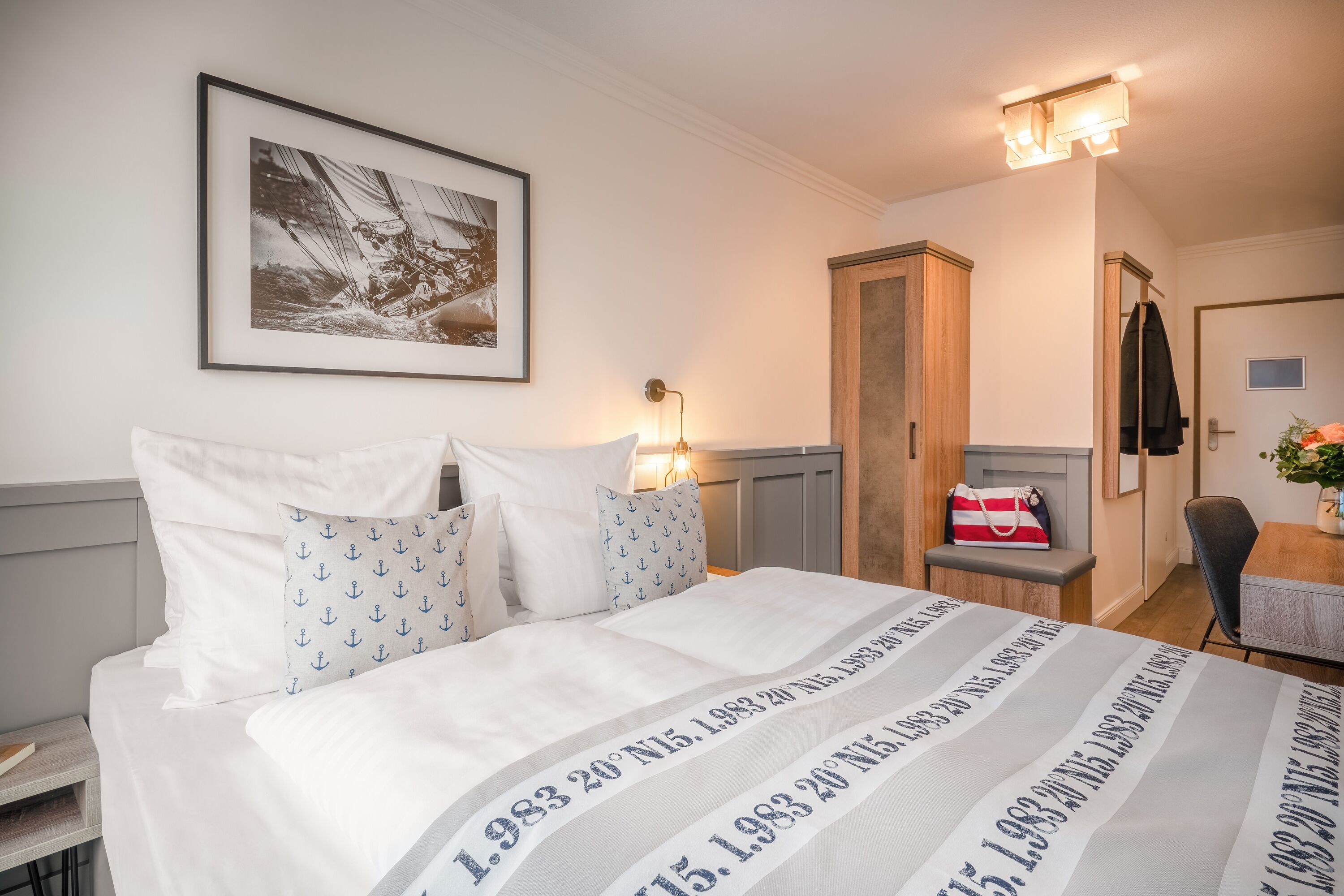 Un lit bien fait, recouvert d’une couvre-lit à rayures, un tableau encadré au mur, une table de chevet avec une lampe et une armoire.