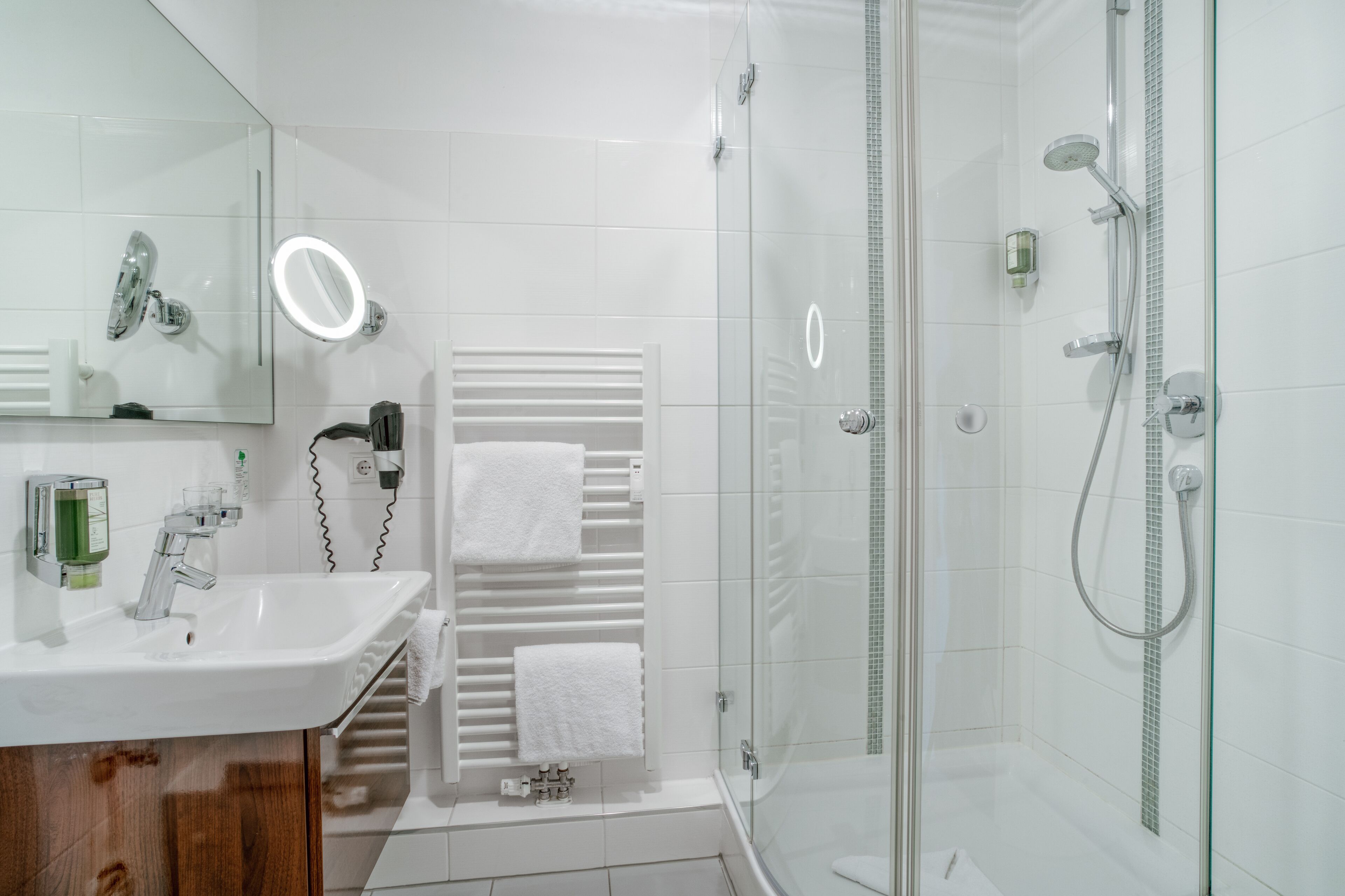 Een moderne badkamer met een douchecabine van glas, een witte wastafel en een spiegel met ingebouwde verlichting.