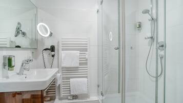 A modern bathroom with a glass-enclosed shower, a white sink, and a mirror with a built-in light.