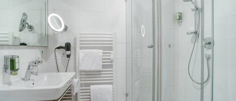 A modern bathroom with a glass-enclosed shower, a white sink, and a mirror with a built-in light.