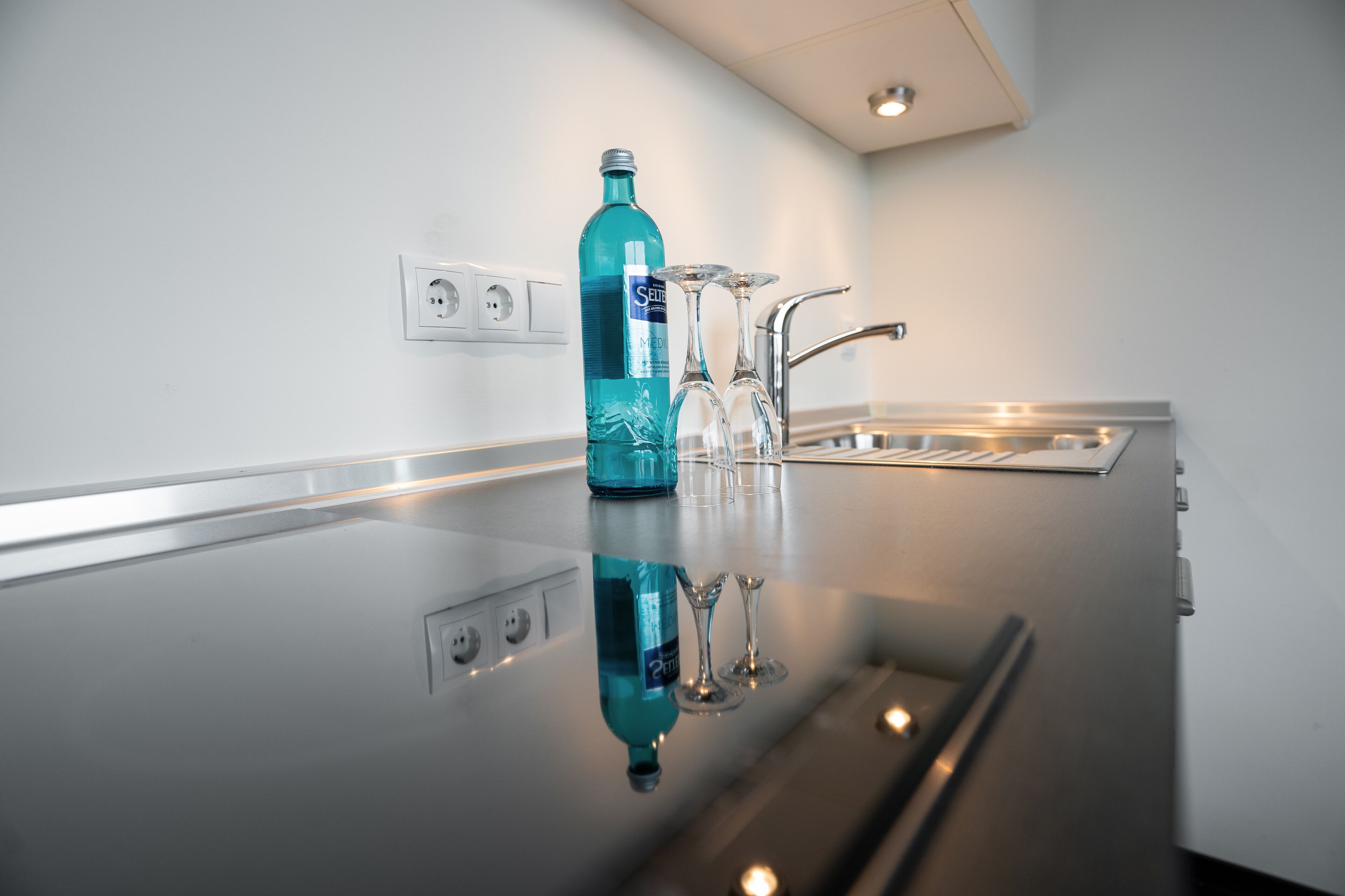 A modern kitchen with a reflective countertop, a bottle of mouthwash, and two wine glasses.