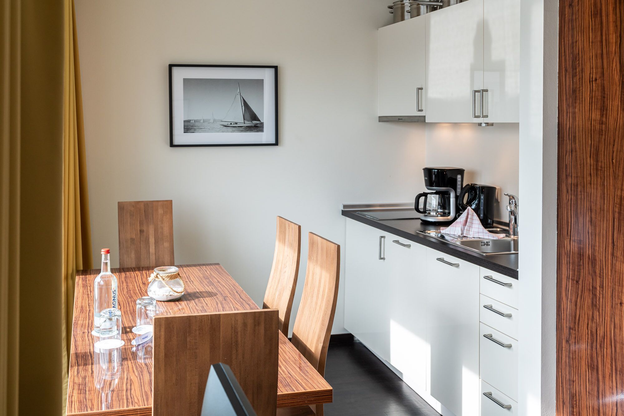 A modern kitchen with white cabinets, a coffee maker, and a framed picture of a sailboat on the wall.