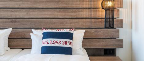 Una habitación de hotel con cabecera de madera, lámpara de noche y almohadas con texto.