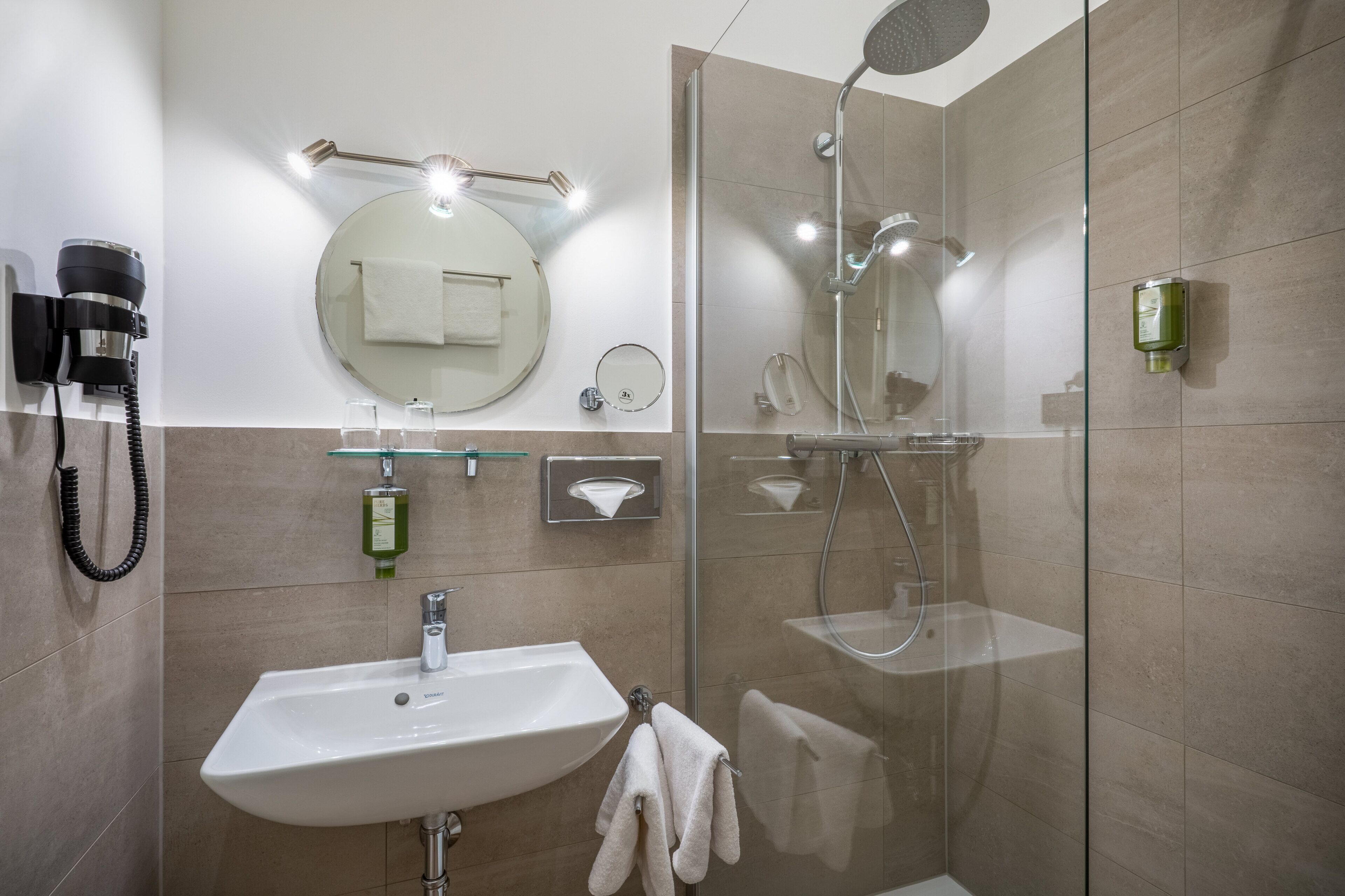 A modern bathroom with a glass-enclosed shower, a sink with a towel, and a hairdryer mounted on the wall.