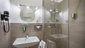 A modern bathroom with a glass-enclosed shower, a sink with a towel, and a hairdryer mounted on the wall.