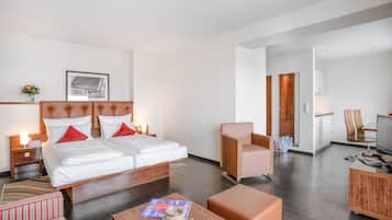 A modern hotel room with a large bed, a sitting area with a coffee table, and a kitchenette.