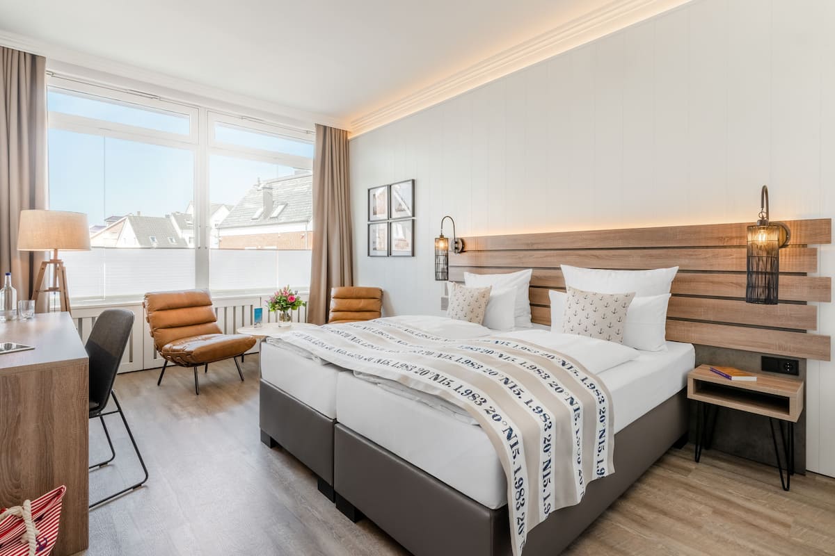 Une chambre d’hôtel avec un grand lit, un bureau, une chaise et une fenêtre donnant sur des immeubles.