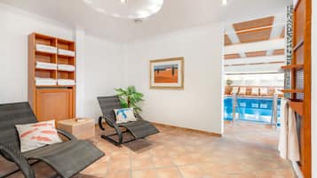 Una habitación con piscina, una silla con cojín, un estante con toallas y un cuadro en la pared.