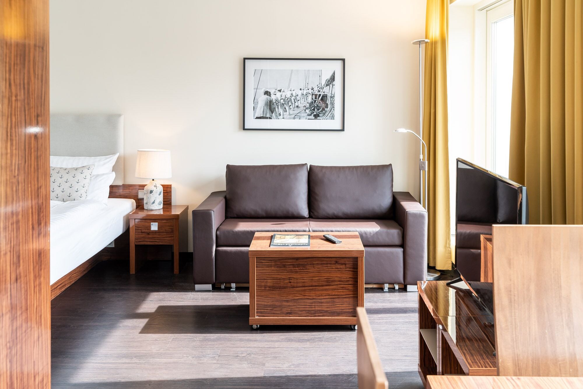 A hotel room with a bed, a sofa, a coffee table, a TV, and a framed picture on the wall.