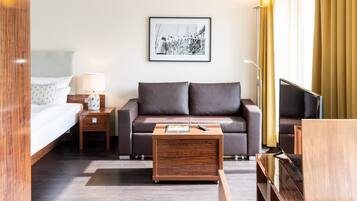 Ett hotellrum med en säng, en soffa, ett soffbord, en tv och en inramad tavla på väggen.
