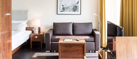Una habitación de hotel con una cama, un sofá, una mesa de centro, un televisor y un cuadro en la pared.