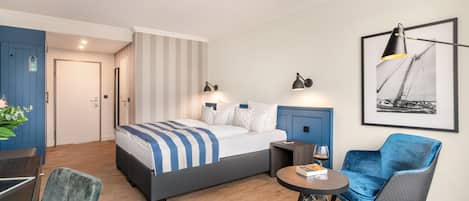 Una habitación de hotel con cama, escritorio, silla, una mesita pequeña y un cuadro en la pared.