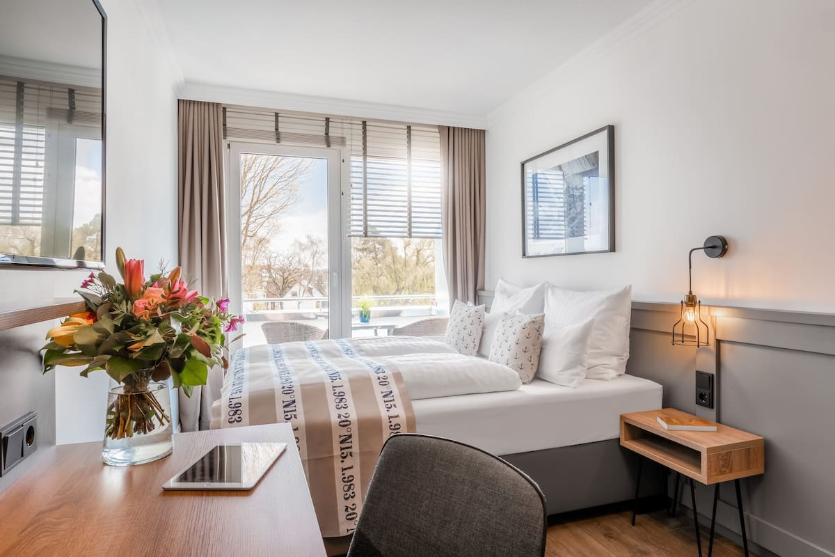 Une chambre d’hôtel moderne, équipée d’un lit, d’une table de chevet, d’une chaise et offrant une vue sur l’extérieur grâce à de grandes fenêtres.