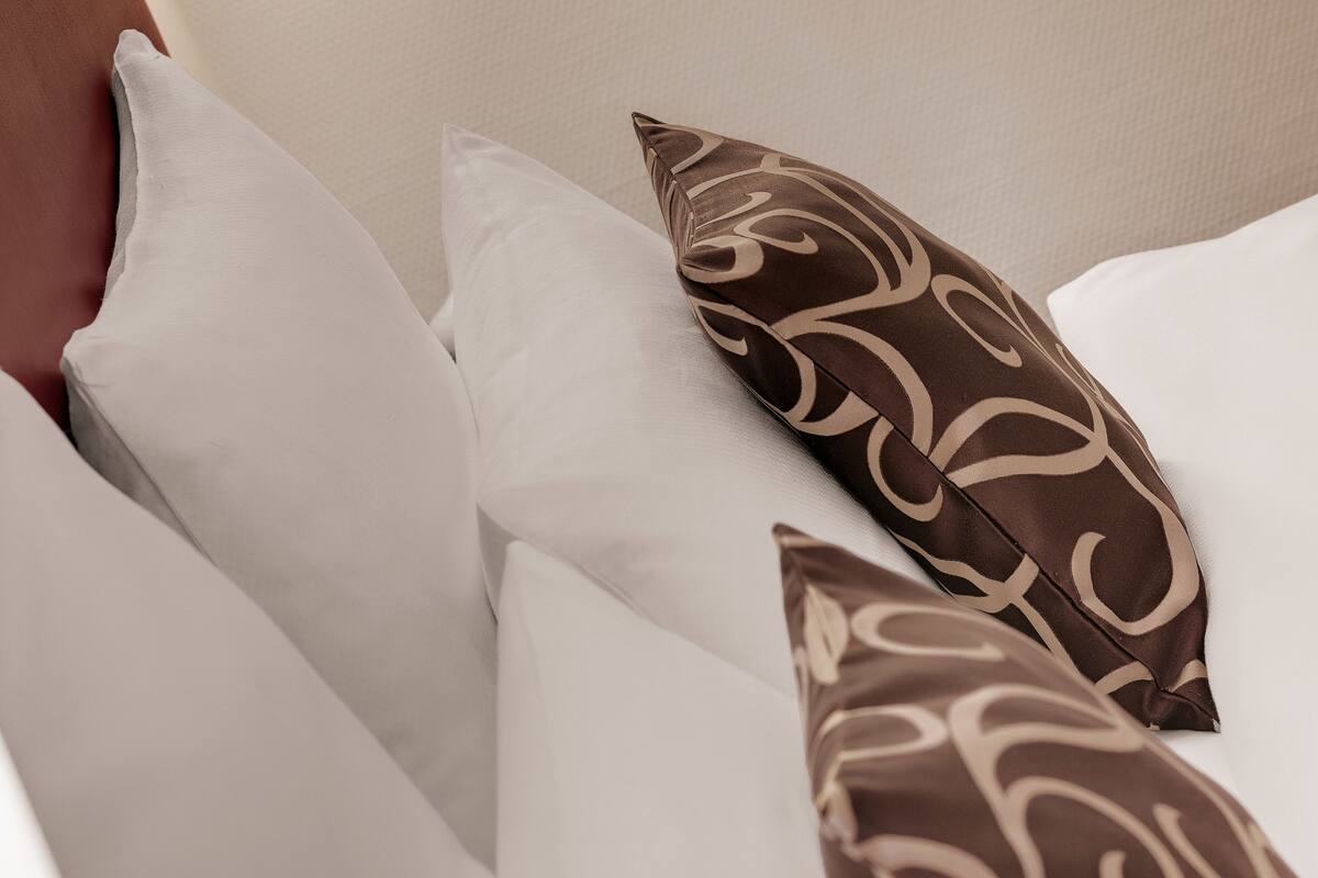 A bed with white and patterned pillows, a wooden headboard, and a wall-mounted light fixture.
