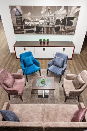 Un salón moderno con un sofá, dos sillones, una mesa de centro y un cuadro grande con un paisaje urbano en la pared.