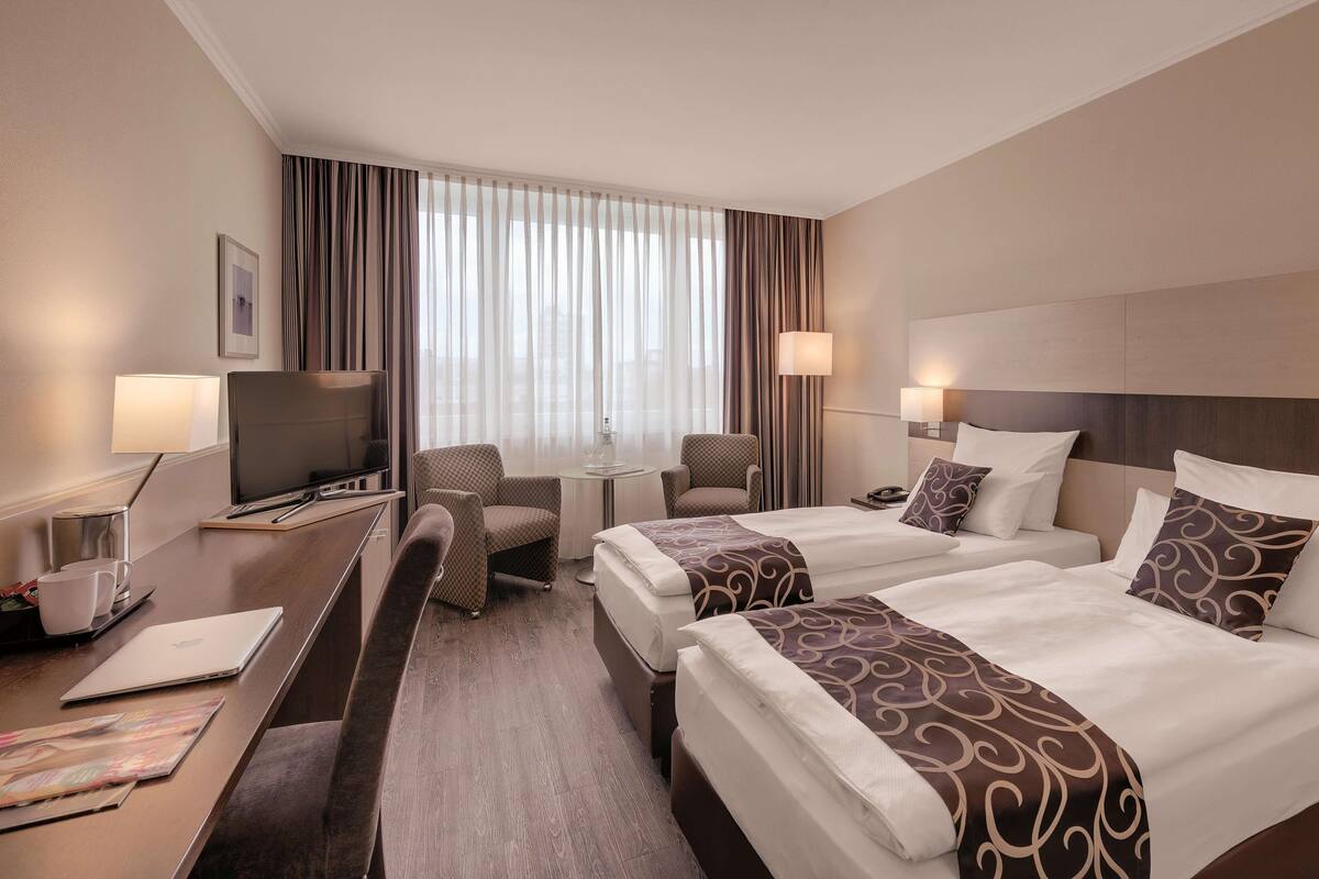 A hotel room with two beds, a desk with a laptop, a TV, and a chair.