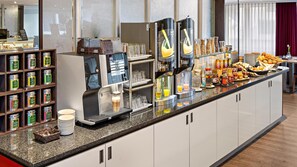 Un mostrador de desayuno autoservicio con máquinas de café, diversas opciones de alimentos y una selección de salsas.