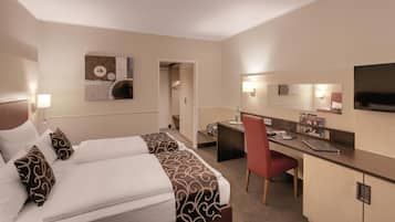 A hotel room with a bed, desk, chair, and a TV.