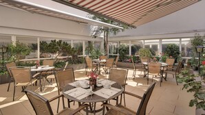 An outdoor patio area with round tables and wicker chairs, surrounded by potted plants and trees. - Best Western Hotel Darmstadt Mitte (Darmstadt)