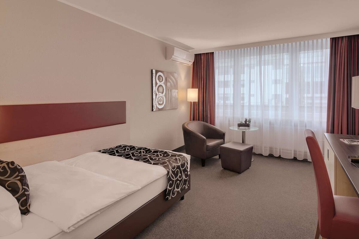 A hotel room with two beds, a desk, a chair, a small table, and a TV.