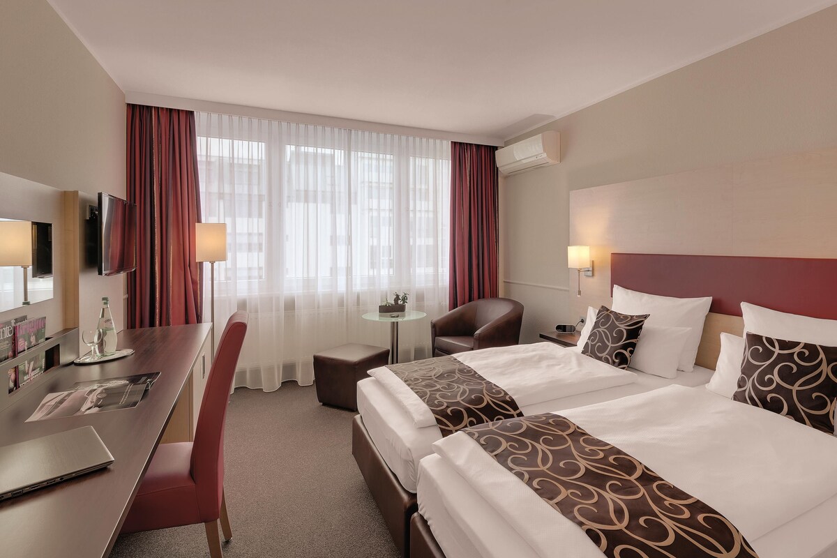 Habitació d'hotel amb llit, escriptori, cadira i televisió.