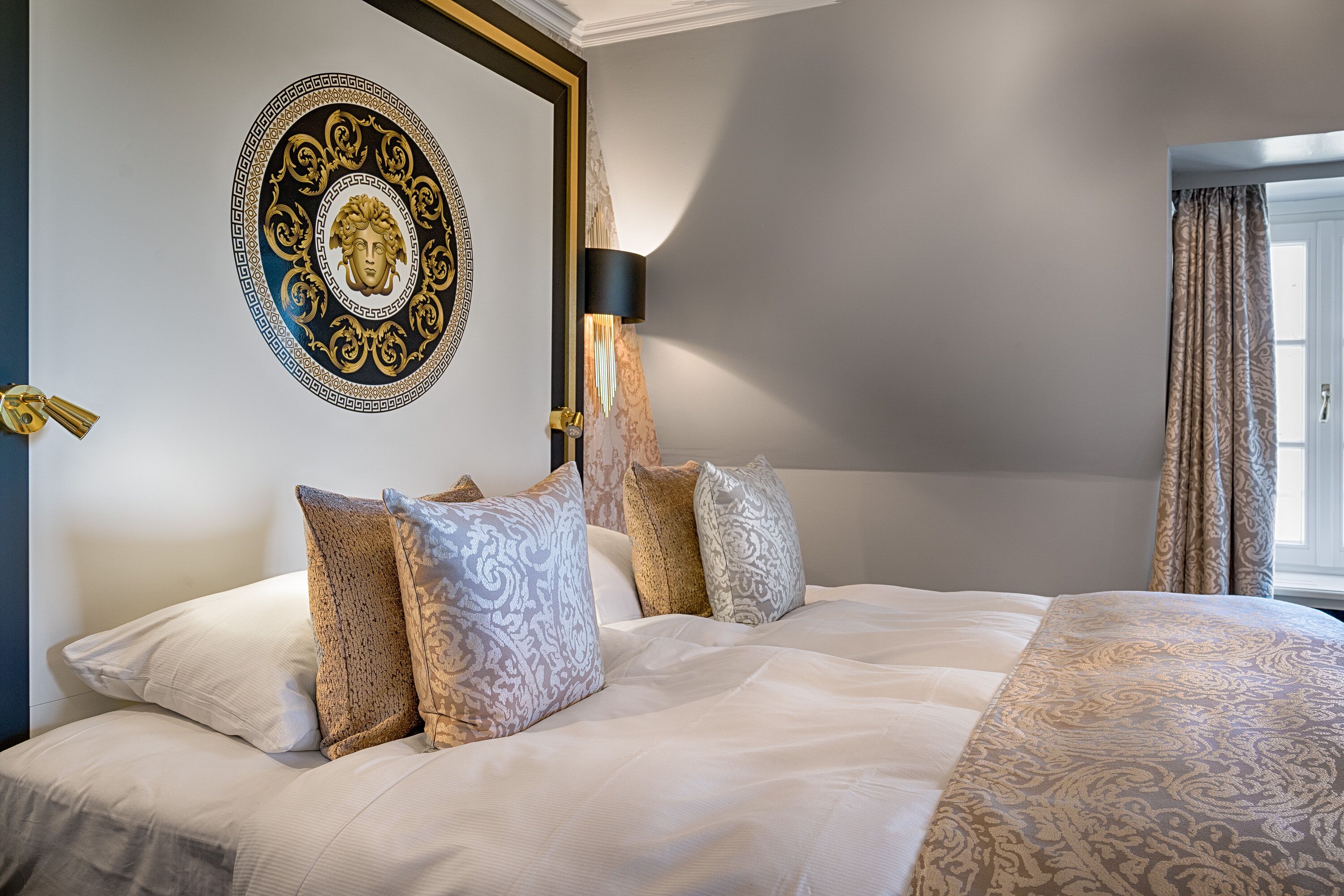 Une chambre d’hôtel avec un grand lit, des œuvres d’art décoratives au mur, une lampe et des rideaux à motifs.