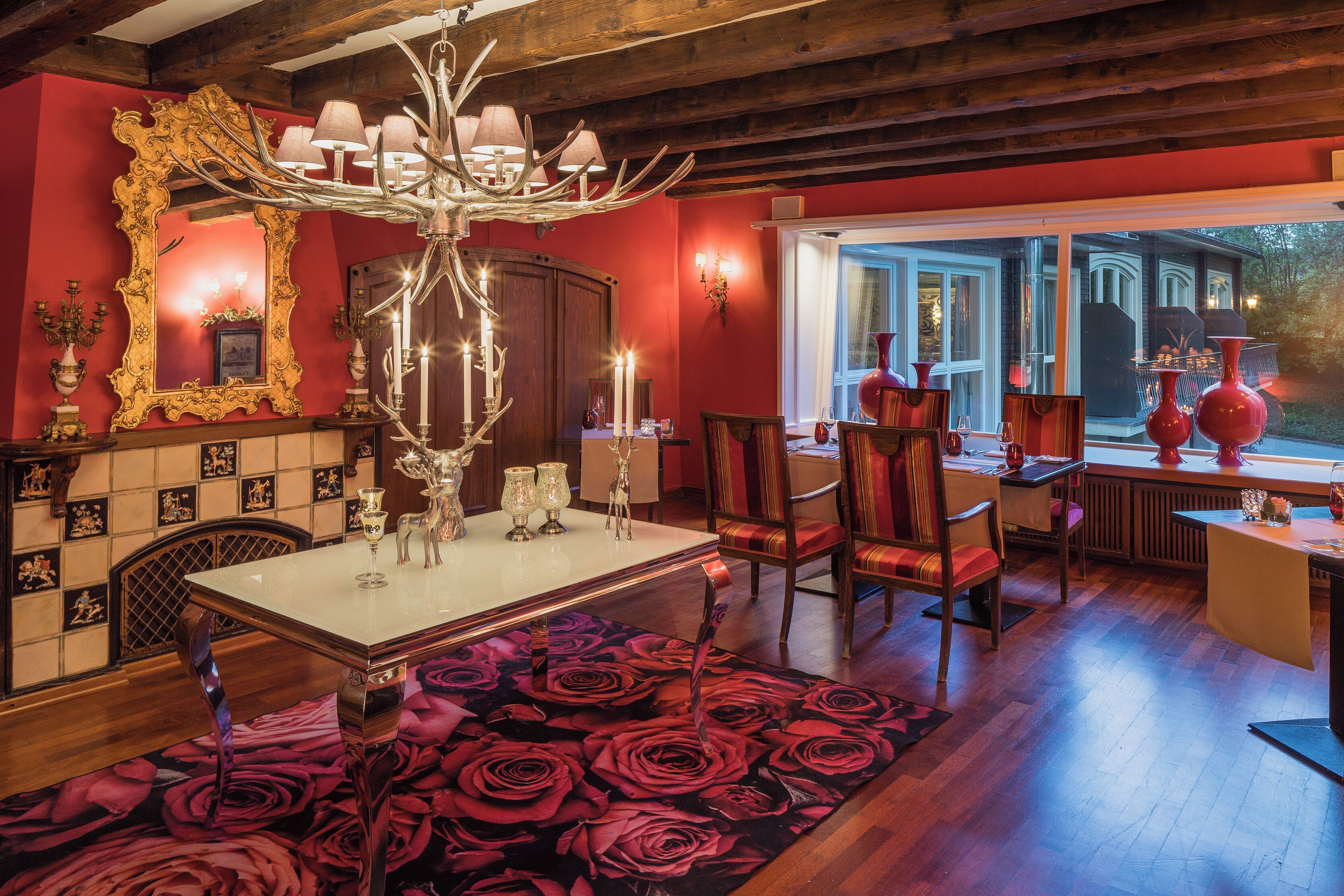 A dining area with a chandelier, red walls, and a large mirror.