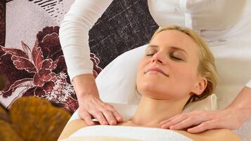 Une personne reçoit un massage, et un mur orné de motifs floraux se trouve derrière elle.