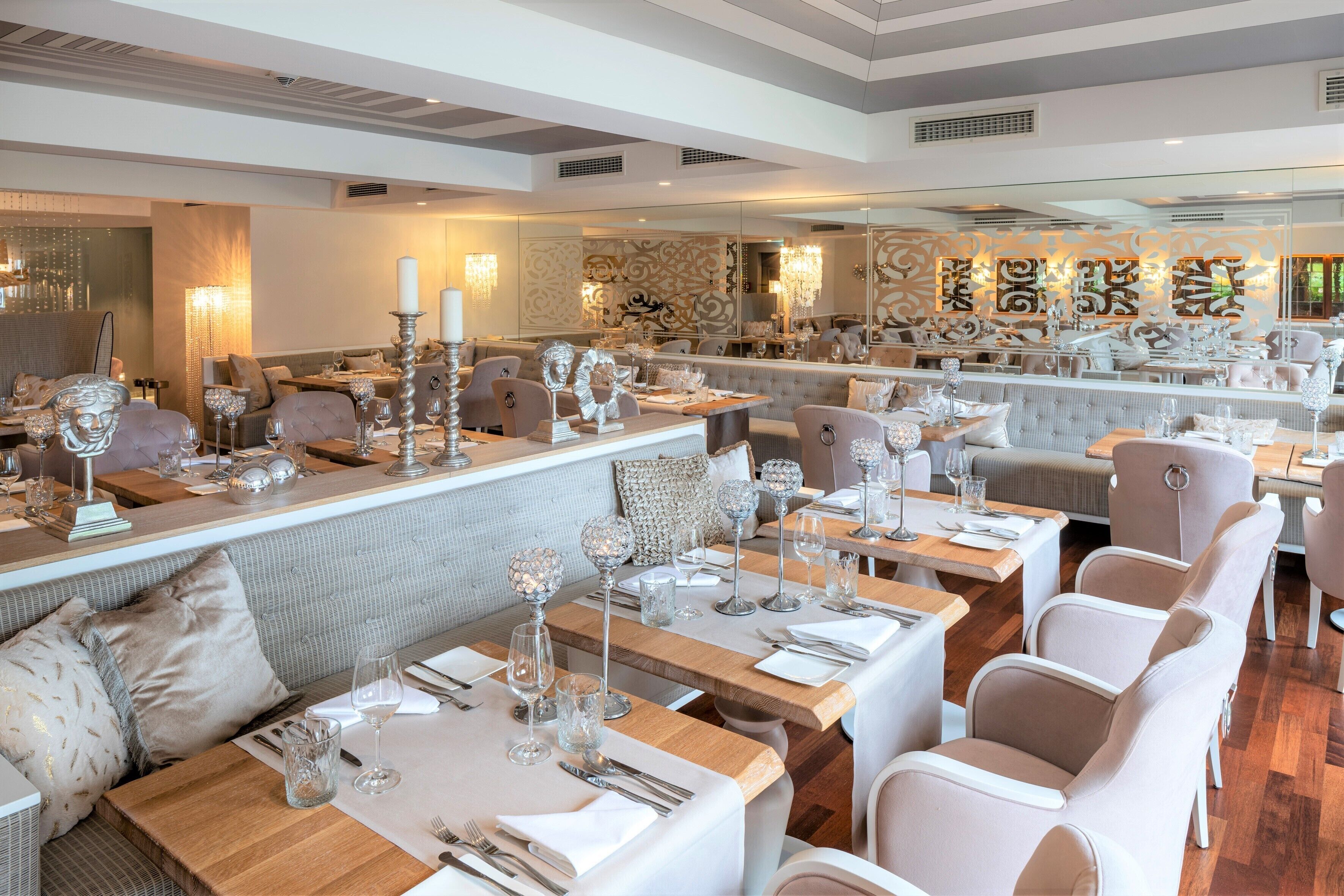 Un restaurante con varias mesas, cada una con mantel blanco, cubertería y copas de vino.