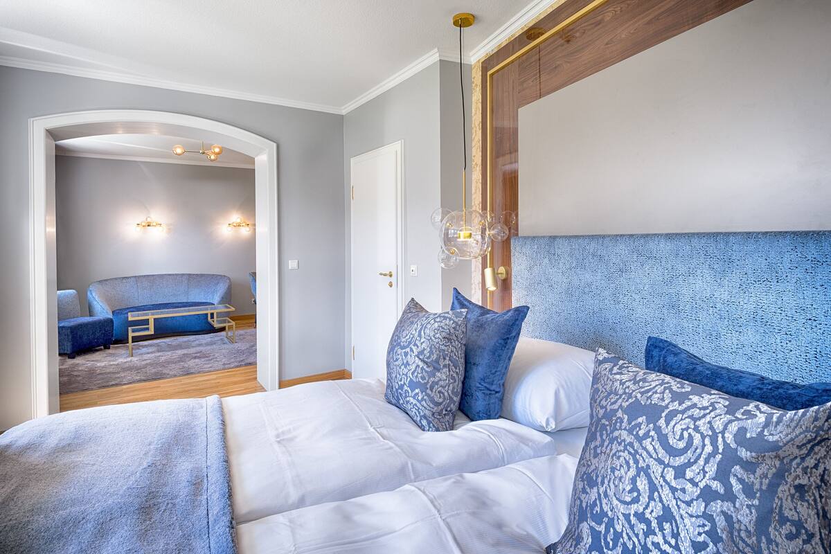Un dormitorio con una cama grande, un cabecero y vistas a otra habitación con un sofá y una mesa.