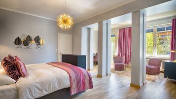 A modern bedroom with a large bed, a TV, and a unique ceiling light. There are two chairs and a window with curtains.