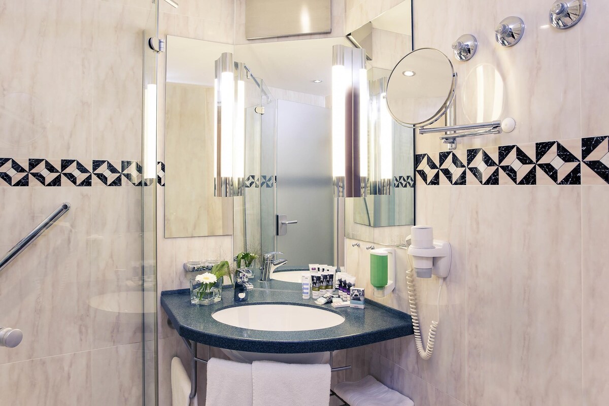 Un baño moderno con cabina de ducha de vidrio, lavabo con artículos de aseo y espejo.