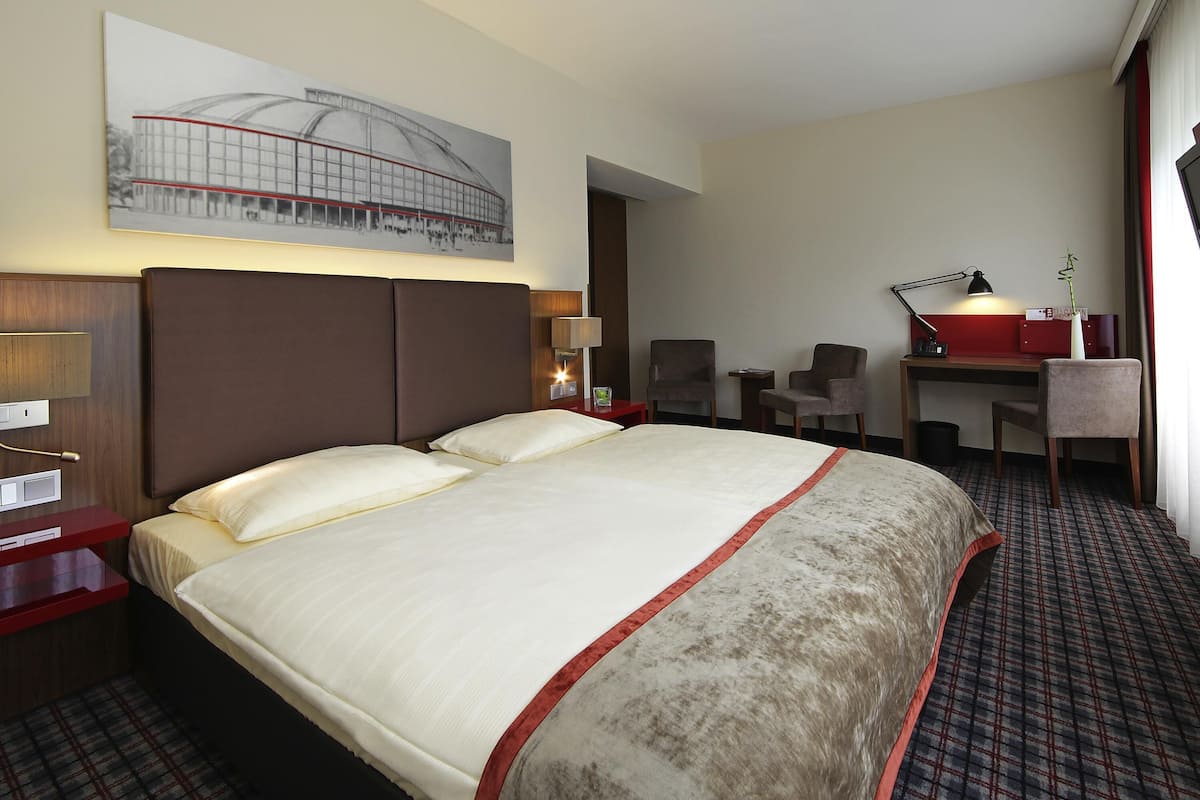 A hotel room with a large bed, two chairs, a desk, and a lamp.