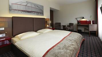 Une chambre d’hôtel avec un grand lit, deux fauteuils, un bureau et une lampe.
