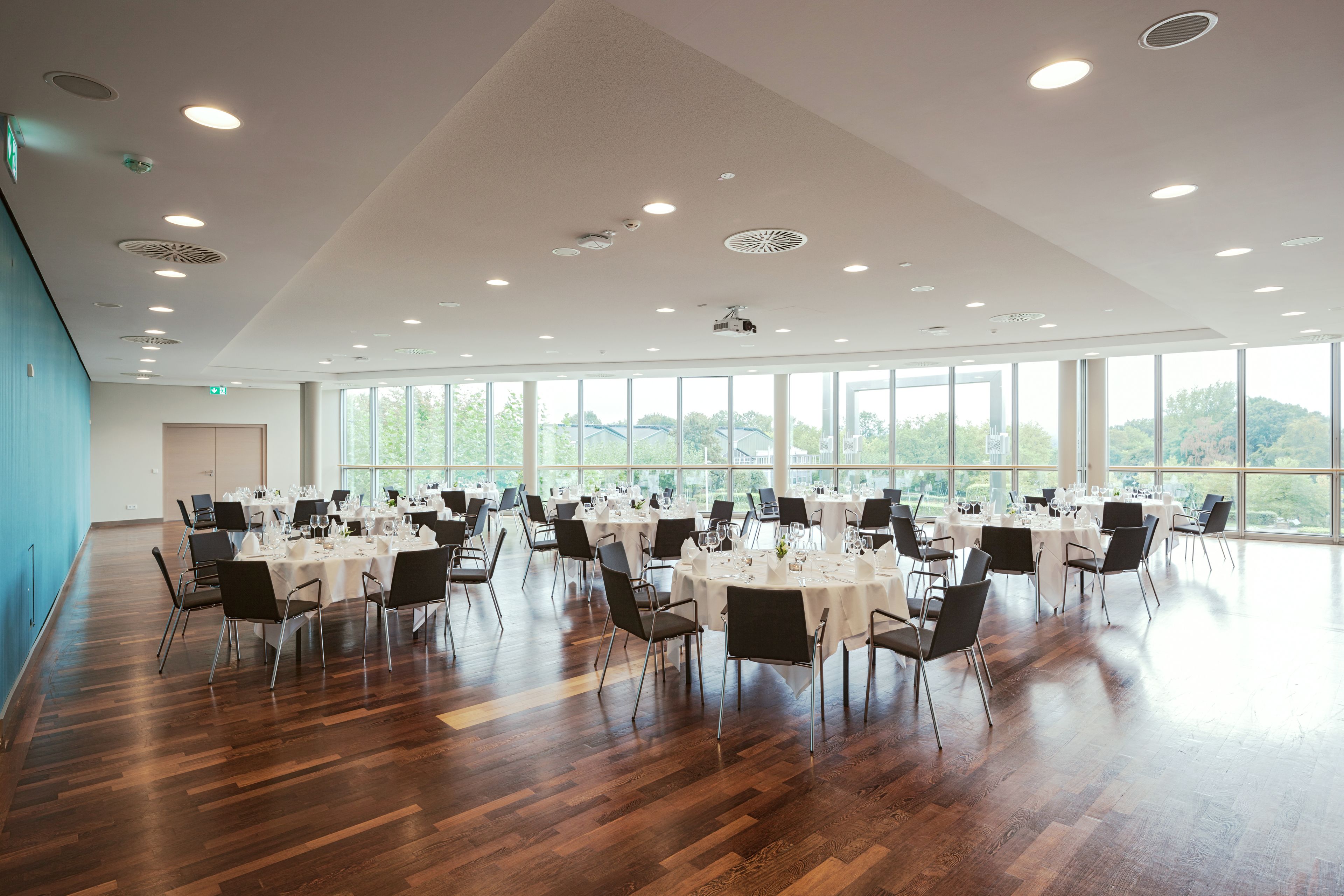 A spacious conference room with round tables, chairs, and a high ceiling with recessed lighting.