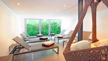 Ein moderner Spa-Bereich mit Massagestühlen, einem großen Fenster mit Blick ins Grüne und einem außergewöhnlichen Hängekorbsessel.