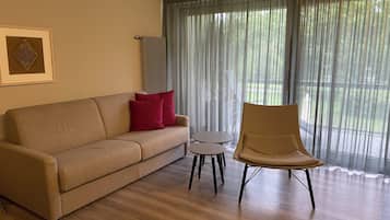 Ein Wohnzimmer mit einem beigefarbenen Sofa, zwei roten Kissen, einem kleinen runden Tisch und einem Sessel.